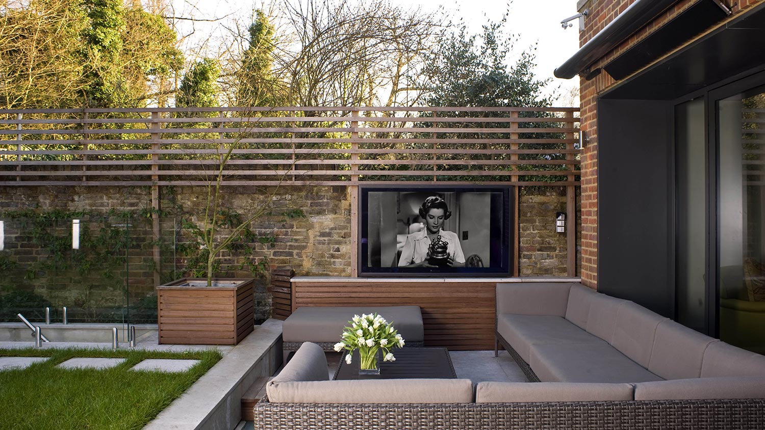 Outdoor seating area with a built-in TV on a garden wall