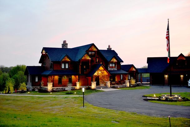 Large timber-style house with lit exterior at dusk, flagpole in front yard