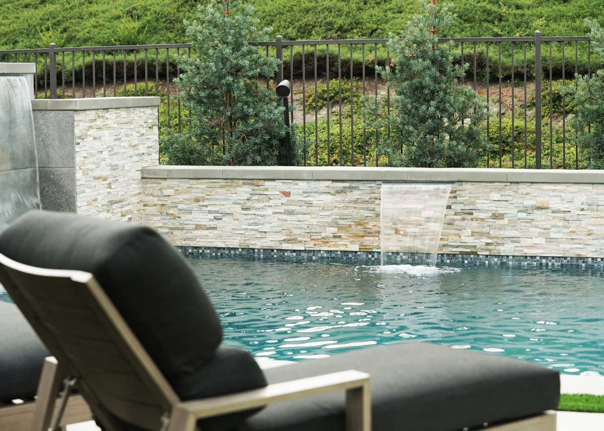Outdoor fire pit with wooden chairs beside a modern pool at dusk