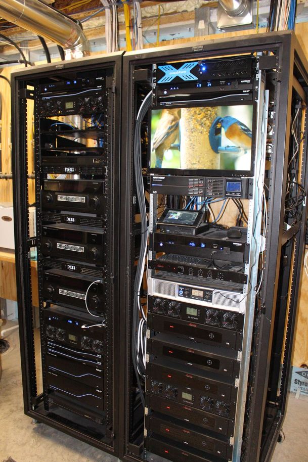 Rack-mounted AV equipment and server gear with a monitor displaying birds at a feeder