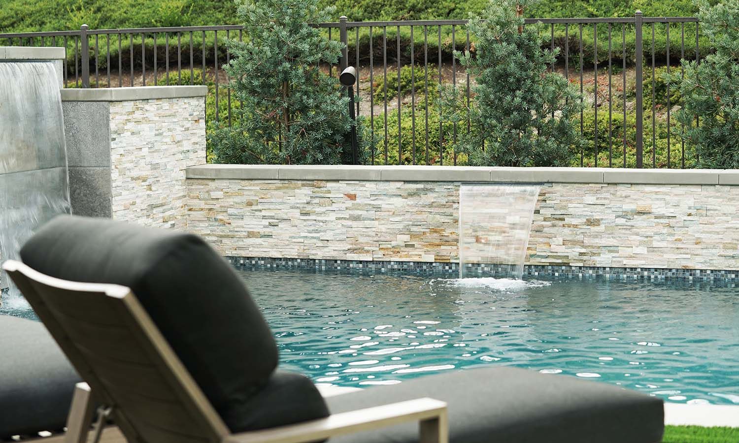 Luxurious outdoor pool with cascading waterfalls, lounge chairs, and lush greenery.
