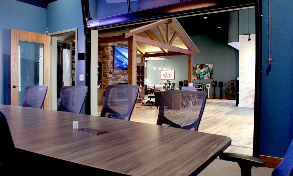 Conference room with wooden table, mesh chairs, and view of showroom beyond