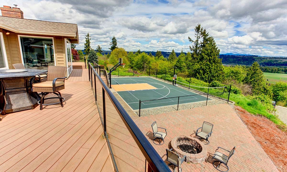 Scenic backyard with a wooden deck, fire pit, and basketball court overlooking lush greenery.