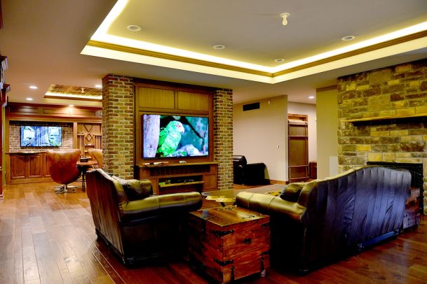 Cozy living area with leather seating, brick and stone accents, and two large wall-mounted TVs
