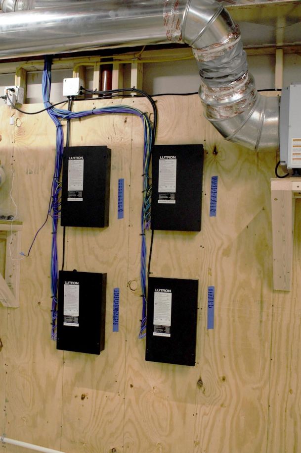 Four Lutron control panels mounted on a plywood board with blue wiring neatly organized