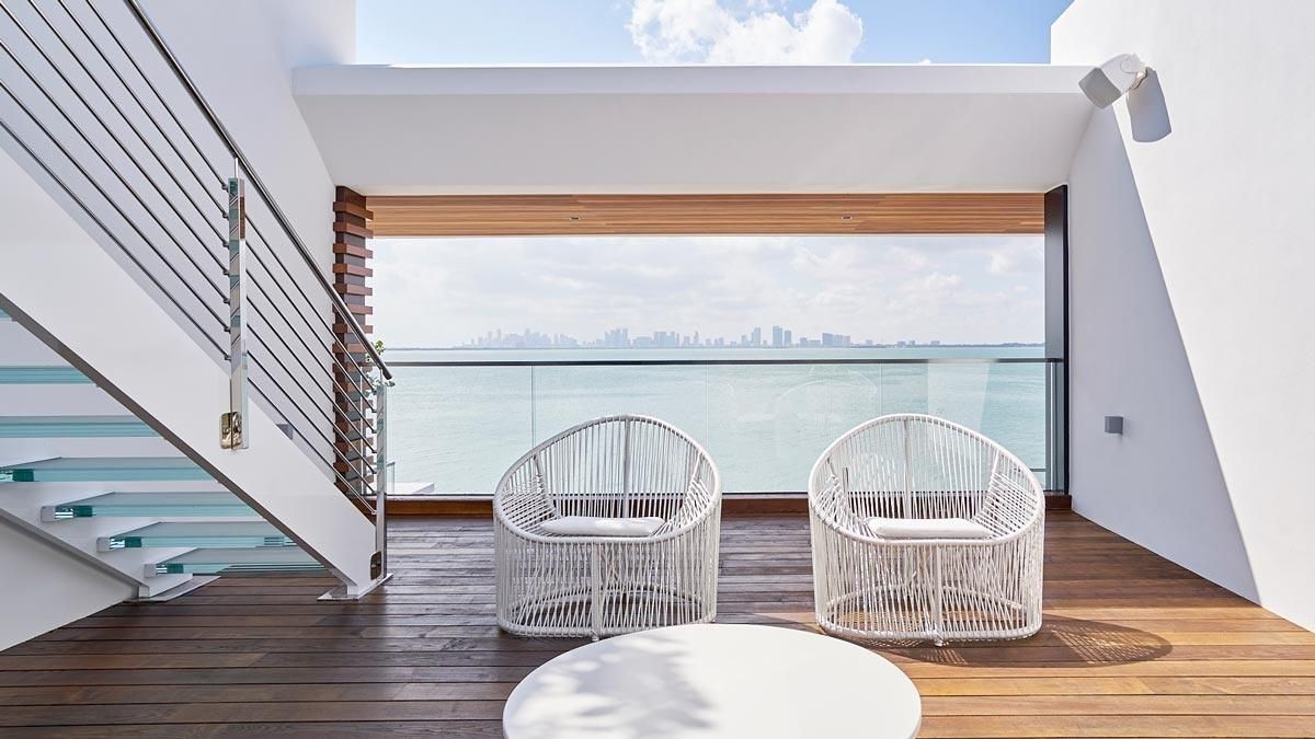 Modern balcony with white chairs overlooking the ocean and city skyline