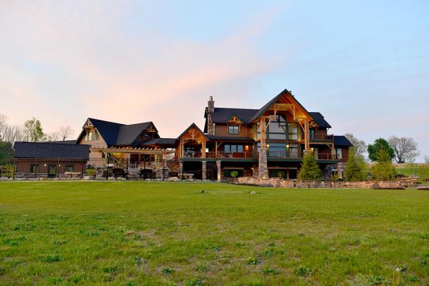 Expansive view of timber estate home with manicured lawn at sunset